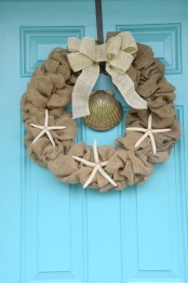 a burlap wreath with a white burlap bow on top and starfish is a cool idea for a rustic beach home at Christmas