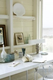 a neutral beach home office with a floating desk and a metal chair, a large shelving unit with beautiful sea decor and a view