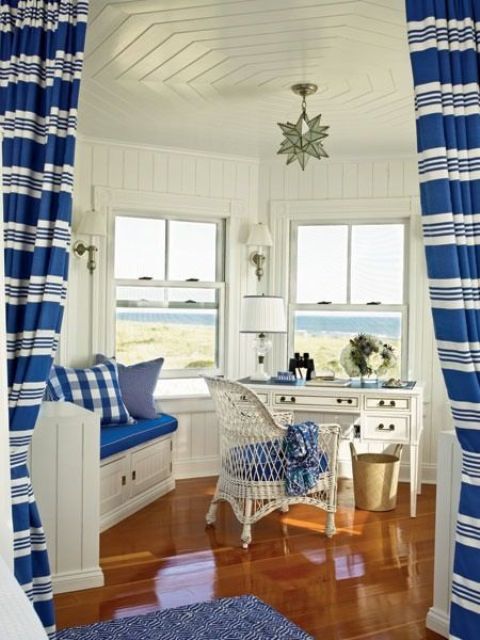 a nautical home office in bold blue and white, with a gorgeous sea view, a white desk and a built in bench and with blue textiles
