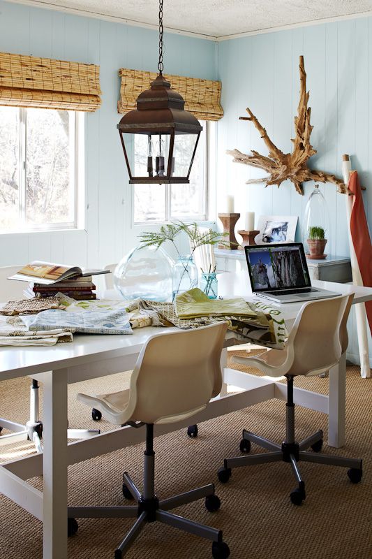 a beach home office with light blue walls, woven shades, a shared desk and chairs, a pendant lamp on chain and a driftwood piece on the wall