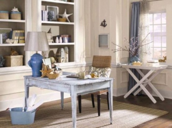 a vintage coastal home office done in neutrals, with built-in shelving units, a blue desk, a mini table and blue textiles
