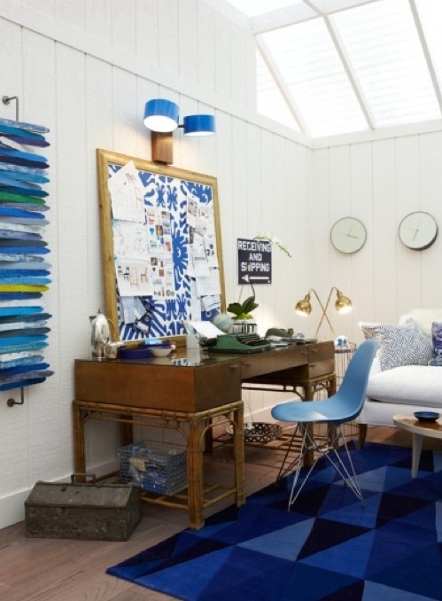 a bright sea-themed home office with white walls, a bold blue rug, art and a memo board plus skylights for more natural light