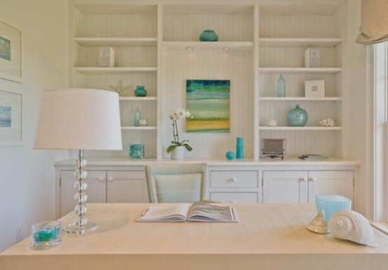 a neutral coastal home office with built-in shelves, a desk, a lamp and touches of aqua and blue