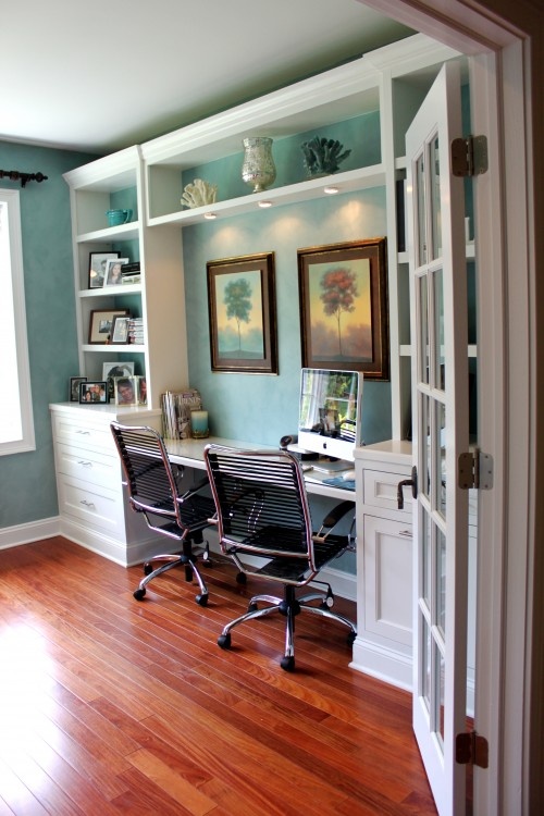 a beach-inspired home office with light blue walls, a white shelving unit for storage and a double built-in desk plus beautiful sea decor