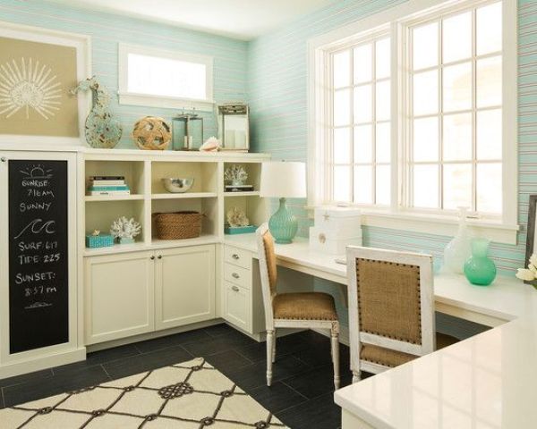 a pretty beachy home office wiht light blue walls, a large white storage unit and a shared desk, beach and sea themed decor