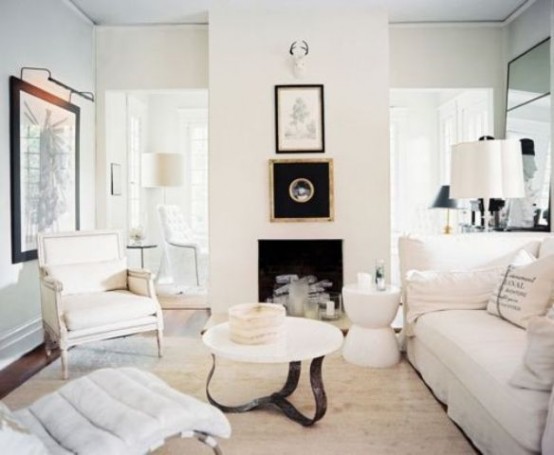 a white living room with a fireplace, elegant seating furniture, cool table and floor lamps and artwork and mirrors around