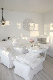a white vintage living room with chic seating furniture, a round table, a vintage clock and a chic chandelier plus blooms
