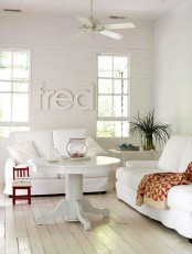 a pretty white living room with white seating furniture, a round table, greenery, a metal coffee table and letters on the wall