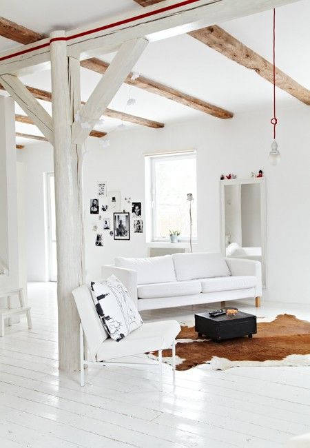 a white living room with a rustic feel, with modern white seating furniture, stained wooden beams, an animal skin rug, a black table