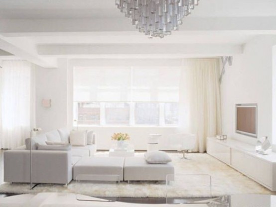 a modern white living room with a neutral sofa, a couple of ottomans and layered rugs, a sleek storage unit and a crystal chandelier