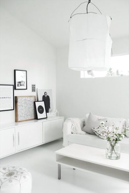 a white Scandinavian living room with a white storage unit, a gallery wall of artwork, a white sofa and a low coffee table, a pendant lamp