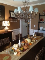a fall or Thanksgiving table runner done with fake bold leaves, neutral pumpkins and some candles