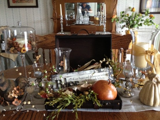 a fall centerpiece of a pumpkin and some greenery, nuts and acorns plus a candle in a tall glass