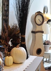 a chic fall arrangement of branches, several white pumpkins and a dried leaf and feather wreath