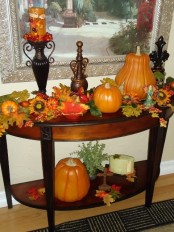 a console styled with faux pumpkins, leaves, gourds and berries plus an orange candle for the fall