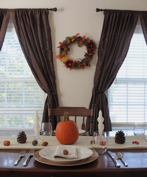 a bright fall wreath on the wall and a table runner with pinecones, nuts and a pumpkin in the center for a fall look