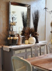 a console in the dining room styled for the fall – with a dried herb wreath, branches, white pumpkins and a stand with pumpkins and faux apples