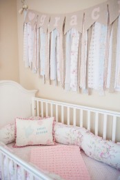 a shabby chic nursery with warm-colored walls, a white crib, pink and floral bedding and a tassel garland over the bed