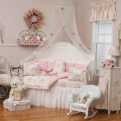 a pink and white shabby chic kid’s room with white furniture, floral bedding and curtains, pink touches and cute toys