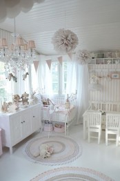 a blush and white shabby chic kid’s room with pink and blush textiles, lamps and garlands, a crystal chandelier, and a metal bed