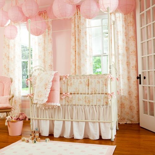 a shabby chic kid's room with pink walls, pink paper lamps, floral bedding and textiles