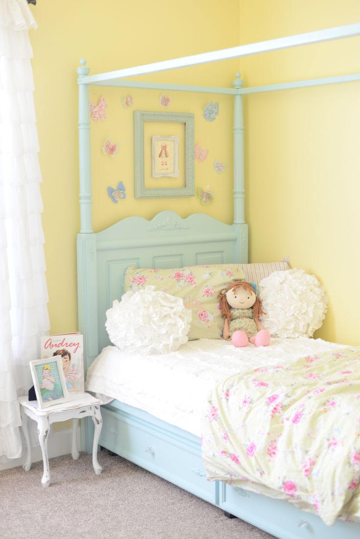 a pastel shabby chic bedroom with yellow walls, a blue bed, floral bedding, empty frames and butterflies is very chic and bright