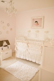 a neutral and blush nursery with vintage furniture, a gallery wall with decorative plates, a crystal chandelier, an artwork