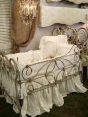a pastel shabby chic kid’s room with lavender walls, a metal crib with white bedding and a crystal chandelier