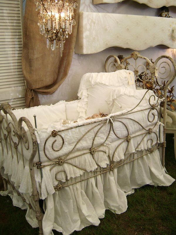 a pastel shabby chic kid's room with lavender walls, a metal crib with white bedding and a crystal chandelier