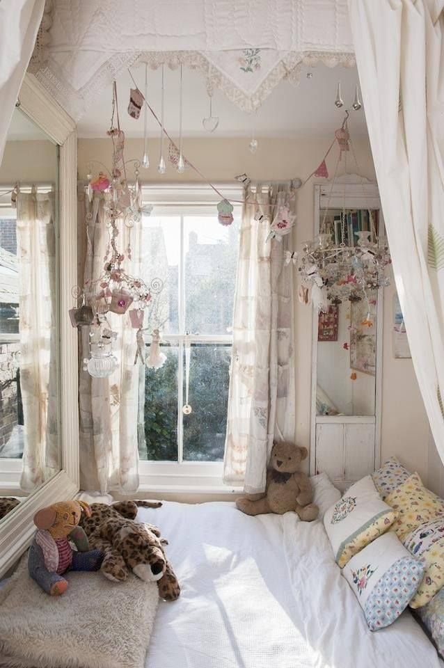 a neutral shabby chic kid's room with a bed by the window, floral bedding and lots of vintage items hung over the bed as decor