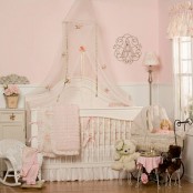 a pink and white shabby chic bedroom with pink walls and white paneling, neutral furniture, floral bedding and lamps and lots of toys