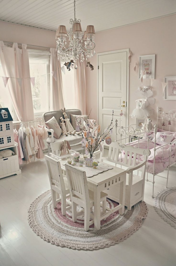 a pink and white vintage meets shabby kid's room with elegant white furniture, a crystal chandelier, pink bedding and curtains, a pretty gallery wall