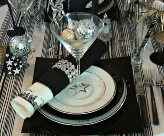 a black, silver and white NYE tablescape with a striped tablecloth, black placemats and napkins, disco balls in a glass is a lovely and shiny solution