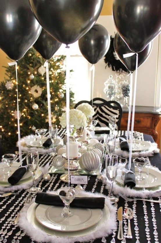a black, silver and white NYE tablescape with a black tablecloth and crystals on it, white faux fur placemats, white porcelain, glasses with silver ornaments and black balloons