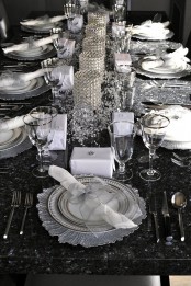 a black and silver NYE party tablescape with shiny metallic chargers, white porcelain, crystals and crystal candleholders as a centerpiece