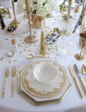 a gold and white NYE tablescape with white blooms, gold candleholders and tall and thin candles, porcelain with gold touches, gold stars on the table