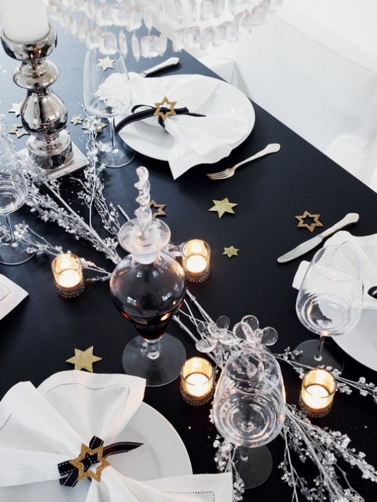 a black and white NYE party tablescape with white porcelain, glasses, candles, silver branches and small stars on the table
