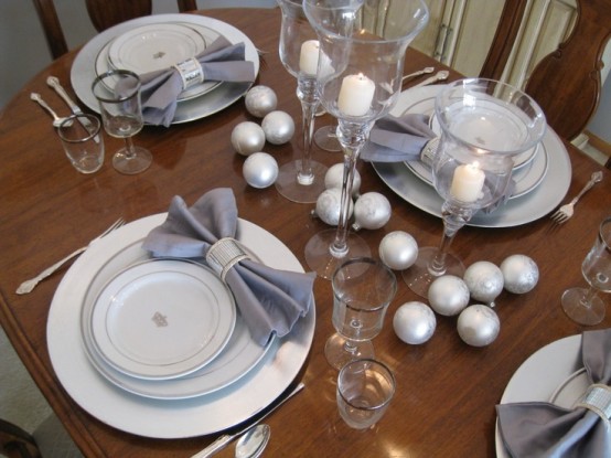 a grey and silver NYE tablescape with matte silver ornaments, silver chargers and grey napkins is an elegant idea