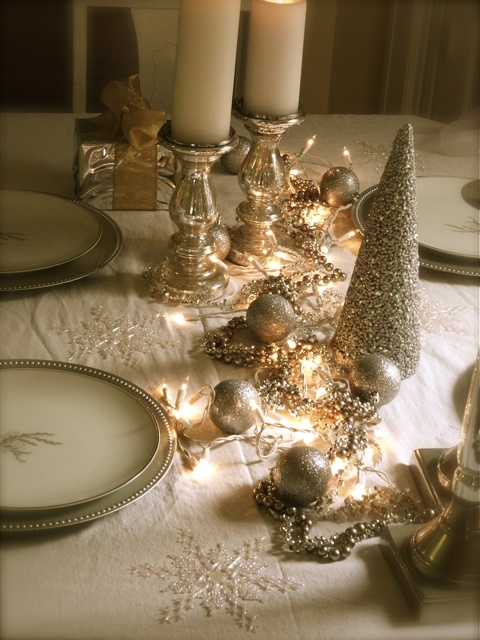 a gold and white NYE tablescape with gold-rimmed glasses, gold glitter ornaments and a cone-shaped tree, candleholders with pillar candles