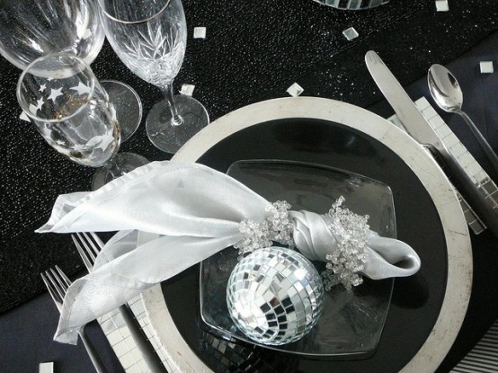 a black and silver NYE party table setting with a silver charger and black plates, silver cutlery and silver stars and squares on the table