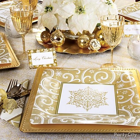 a gold and white NYE tablescape with printed plates, white blooms in a gold vase, gold glasses and napkins