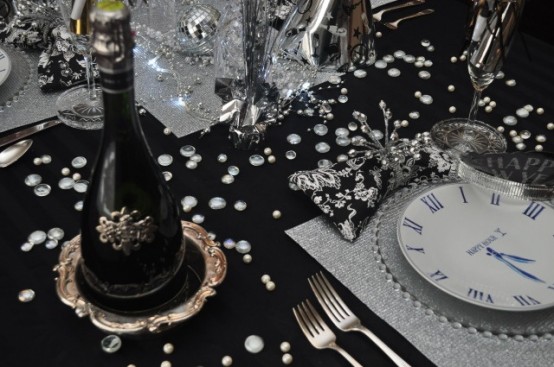 a black and silver NYE party tablescape with silver glitter placemats, a table runner and silver cutlery, rhinestones and disco balls on the table