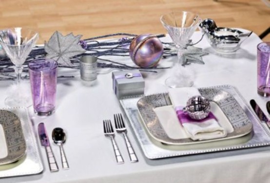 a white, silver and lilac NYE tablescape with silver chargers and cutlery, silver branches and leaves, purple glasses and ornaments