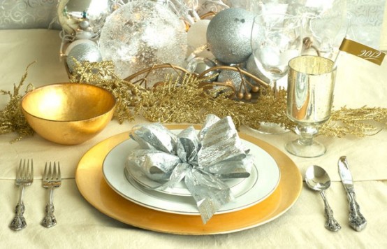 a gold and silver NYE tablescape with a gold charger and bowl, a gold bowl with silver glitter ornaments, silver cutlery and silver beads