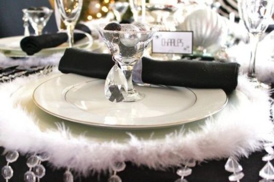 a black and white NYE party tablescape with a faux fur placemat, white porcelain, black napkins and silver ornaments is a stylish idea