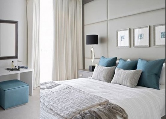 a light grey bedroom with bold blue pillows and a little ottoman to add color