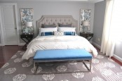 a light grey bedroom spruced up with bold blue pillows, a bench and artworks