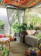 a bright boho patio done with boho rpitned furniture, rugs and a canopy plus lots of potte greenery and plants