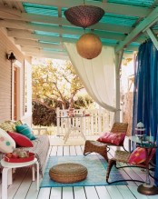 a colorful boho patio with bright pillows and curtains, lanterns and a jute ottoman and a colorful printed rug