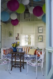a patio done with colorful paper lanterns, white furniture with floral upholstery, colorful pillows and blooms